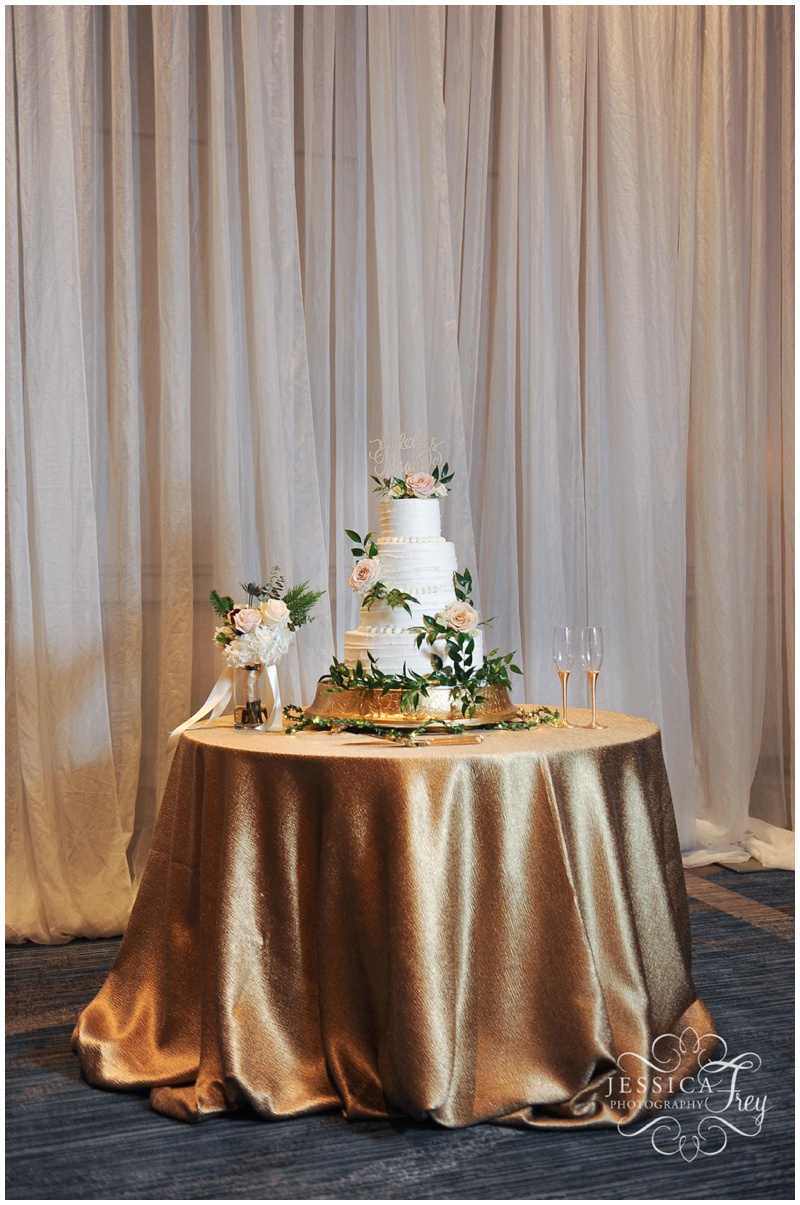 Wedding cake in white with pink flowers and greenery on shimmery gold tablecloth 