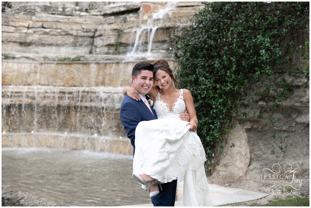 grooms swoops bride up in his arms in front of waterfall at Austin Texas wedding