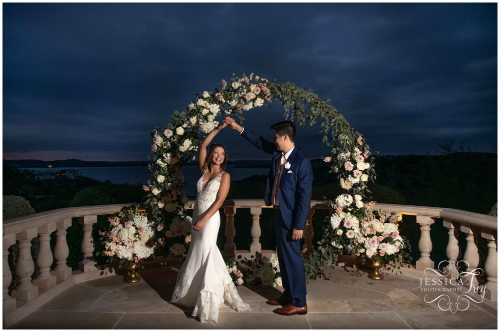 Groom spins his bride at night in front of floral arch at Villa Del Lago